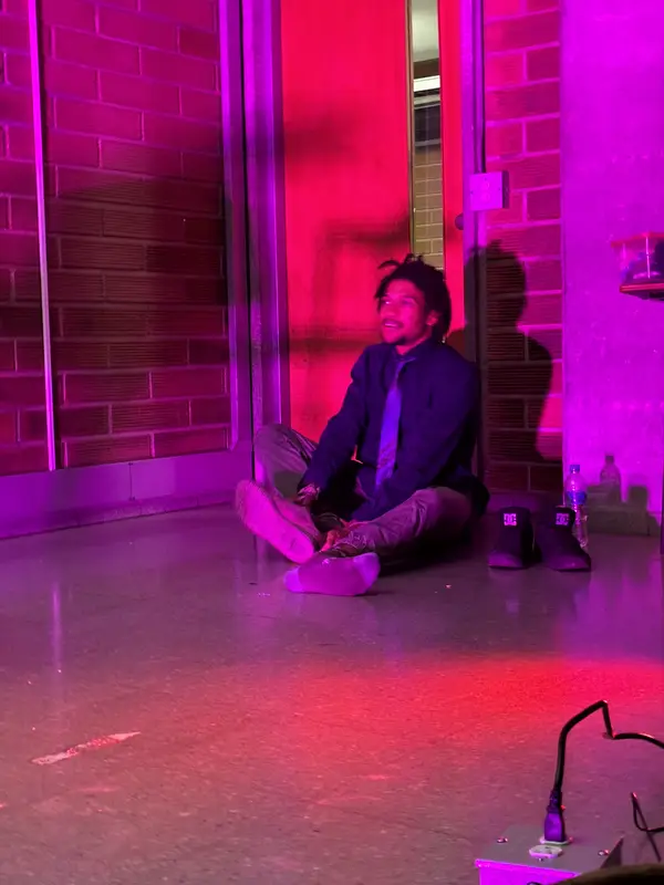 Un actor de traje sentado en el suelo bajo luz roja en el ensayo general