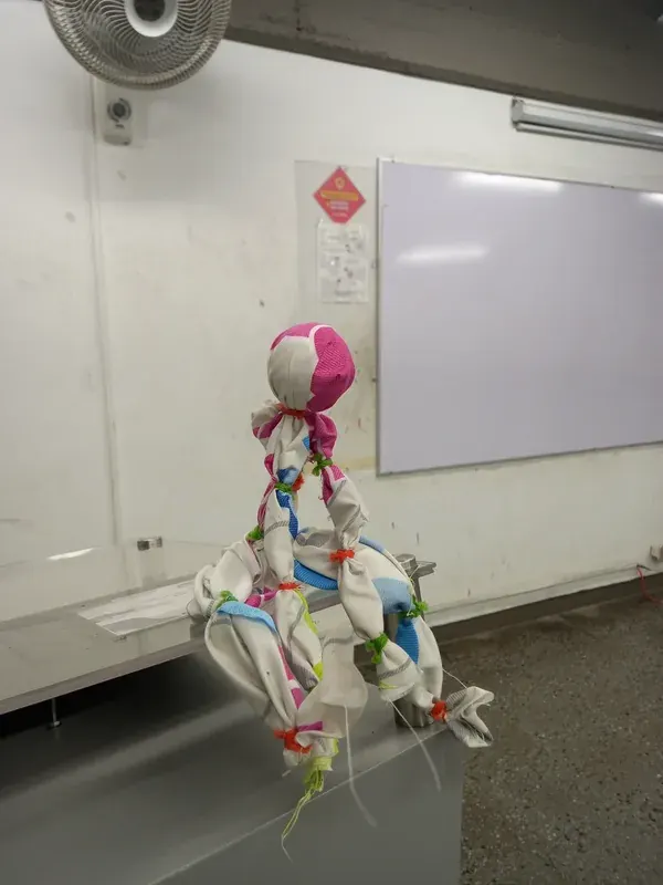 Una muñeca de tela anudada con cintas de colores, creada en el taller, sentada sobre una mesa