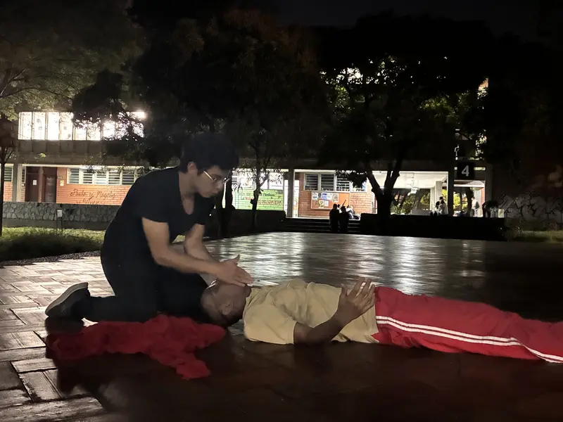 Ejercicio nocturno en la plaza: un integrante tendido sobre una tela roja y otro arrodillado a su lado