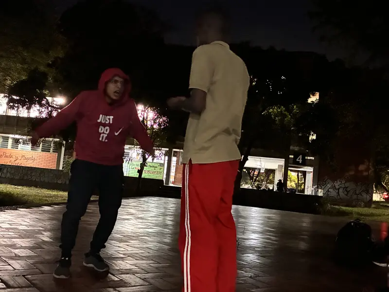 Dos integrantes improvisan frente a frente en la plaza de la universidad, de noche