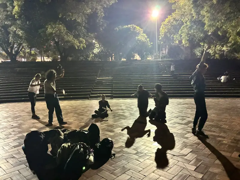 Siluetas del grupo en movimiento bajo los faroles de una plazoleta, de noche